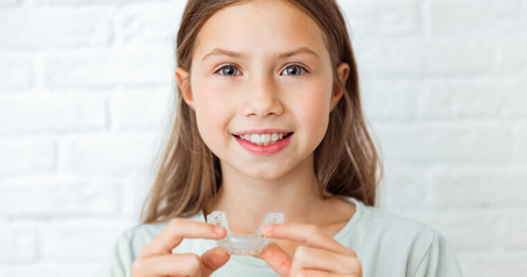 child holding an Invisalign aligner while smiling